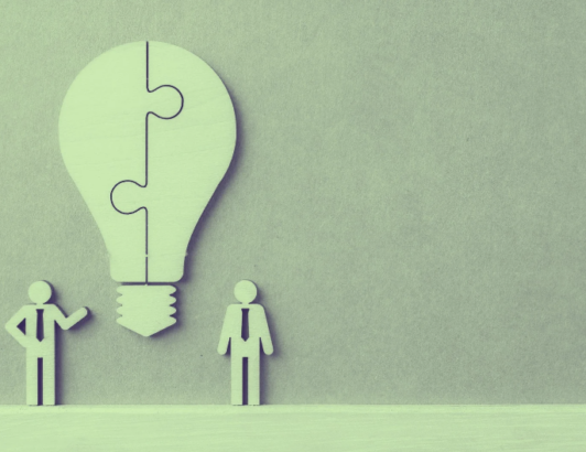 Abstract silhouettes beside a puzzle-piece lightbulb symbolizing teamwork and creative problem-solving.